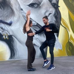Tanztrainer Yuri tanzt mit Nadine Salsa vor einer Graffitiwand.