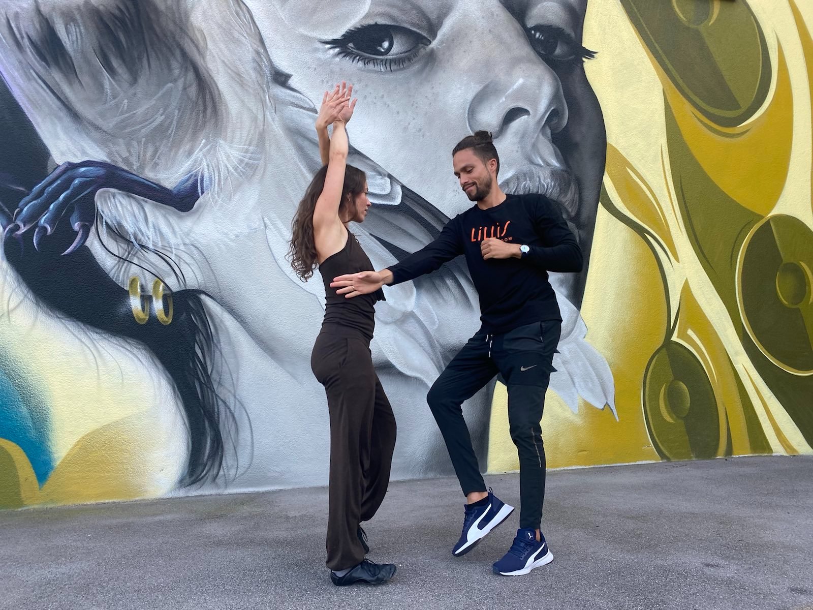 Tanztrainer Yuri tanzt mit Nadine Salsa vor einer Graffitiwand.